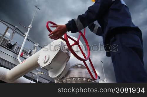 worker closes ball valve on cooling installations at gas compressor station, against background of thunderstorm sky, closeup