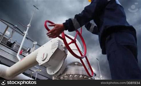 worker closes ball valve on cooling installations at gas compressor station, against background of thunderstorm sky, closeup