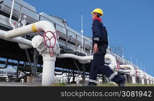 worker closes ball valve on cooling installations at gas compressor station, against background of blue sky