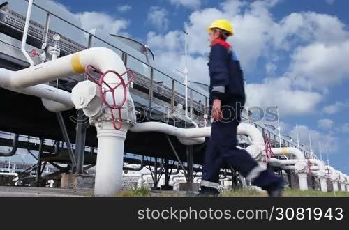 worker closes ball valve on cooling installations at gas compressor station, against background of cloudy sky