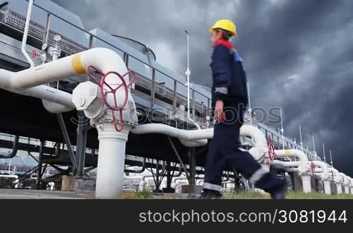 worker closes ball valve on cooling installations at gas compressor station, against background of thunderstorm sky