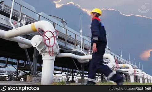 worker closes ball valve on cooling installations at gas compressor station, against background of sunset