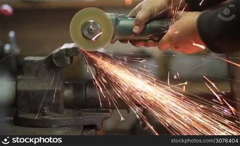Worker cutting metal shaft clamped in a vise with circular saw. Worker cutting metal with grinder with many sharp sparks.