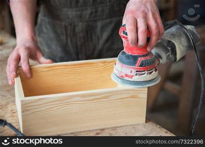 Worker grinds the wood box of angular grinding machine. Profession, carpentry and woodwork concept.. Worker grinds the wood box
