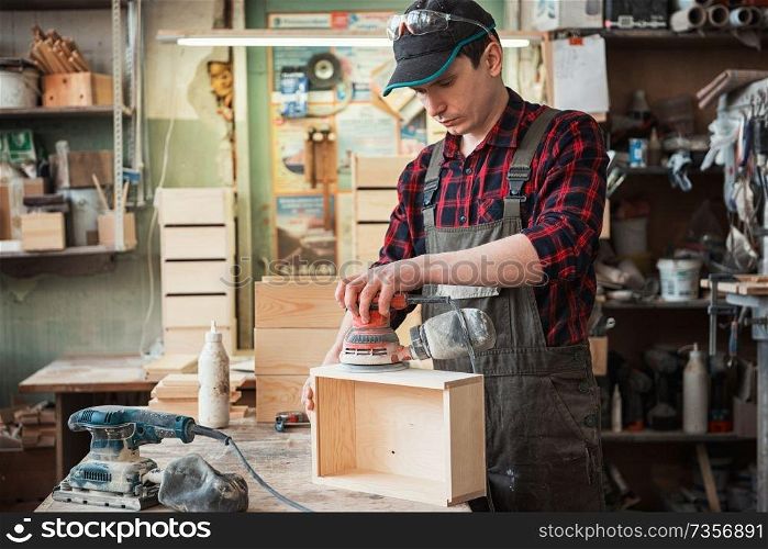 Worker grinds the wood box of angular grinding machine. Worker grinds the wood box