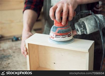 Worker grinds the wood box of angular grinding machine. Worker grinds the wood box