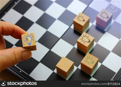 worker hand holding wood block with light bulb gear icon in hand with blur chess board background, idea strategy working