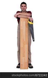 Worker holding a saw and leaning against a wooden plank