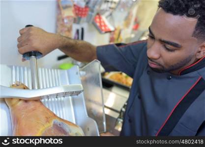 Worker holding cured pork on to slicing machine