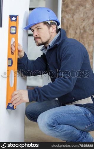 worker in blue uniform measures wall with a level