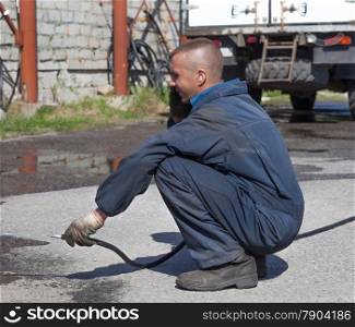 Worker in overalls watering the paved area with water