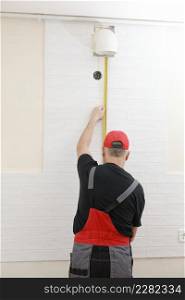 Worker in red cap and work suit with the measuring tape in the kitchen. Man measures the distance, tiler laying a white tile. Repairs in the apartment.. Worker in red cap and work suit with the measuring tape in the kitchen. Man measures the distance, tiler laying a white tile. Repairs in the apartment