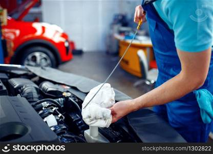 Worker in uniform checks the engine oil level, car service station. Automobile checking and inspection, professional diagnostics and repair. Worker checks the engine oil level, car service