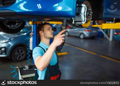 Worker in uniform checks vehicle suspension on lift, car service station. Automobile checking and inspection, professional diagnostics and repair. Worker checks vehicle suspension, car service