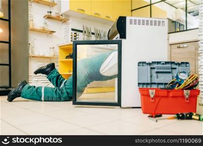 Worker in uniform climbed inside the refrigerator at home. Repairing of fridge occupation, professional service