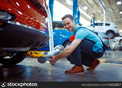 Worker in uniform connects the exhaust gas ventilation system, car service station. Automobile checking and inspection, professional diagnostics and repair. Worker connects the exhaust gas ventilation system