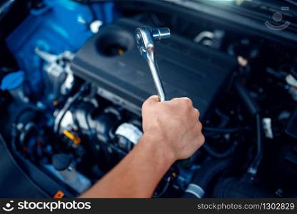 Worker in uniform disassembles vehicle engine, car service station. Automobile checking and inspection, professional diagnostics and repair. Worker disassembles vehicle engine, car service