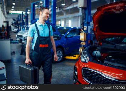 Worker in uniform holds a toolbox, car service station. Automobile checking and inspection, professional diagnostics and repair. Worker holds a toolbox, car service station