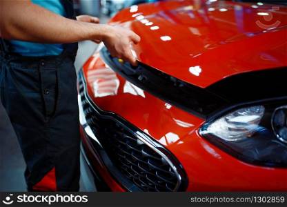 Worker in uniform opens vehicle hood, car service station. Automobile checking and inspection, professional diagnostics and repair. Worker in uniform opens vehicle hood, car service