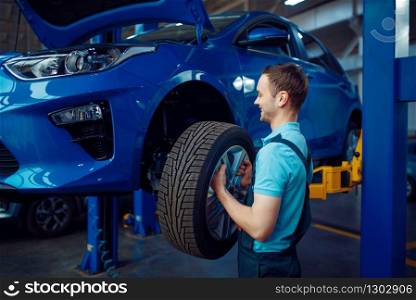 Worker in uniform removes wheel from vehicle, car tire service station. Automobile checking and inspection, professional diagnostics and repair. Worker removes wheel from vehicle, car service