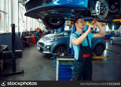 Worker in uniform repairing vehicle on lift, car service station. Automobile checking and inspection, professional diagnostics and repair. Worker repairing vehicle on lift, car service