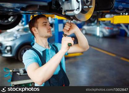 Worker in uniform repairing vehicle on lift, car service station. Automobile checking and inspection.. Worker repairing vehicle on lift, car service