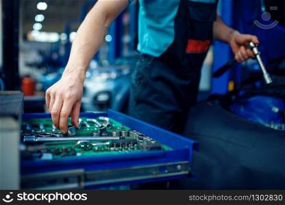 Worker in uniform takes wrench from toolbox, car service station. Automobile checking and inspection, professional diagnostics and repair. Worker takes wrench from toolbox, car service