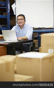 Worker In Warehouse Wearing Headset And Using Laptop