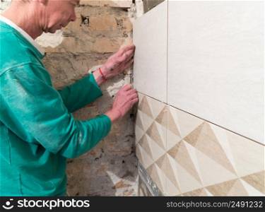 Worker inserts plastic crosses in the seam between tiles. Finishing works, blurred focus. The technology of laying tile.. Repair and finishing works