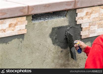 Worker Installing Wall Tile Cement with Trowel and Tile at Construction Site.
