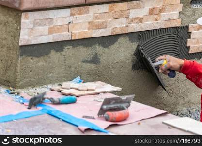 Worker Installing Wall Tile Cement with Trowel and Tile at Construction Site.