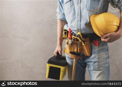 Worker man holding construction helmet and toolbox near wall. Male hand and tools for house room renovation. Home renovation concept