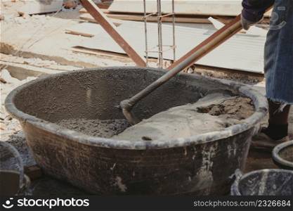 Worker man house builder mix mortar from a trough in bucket