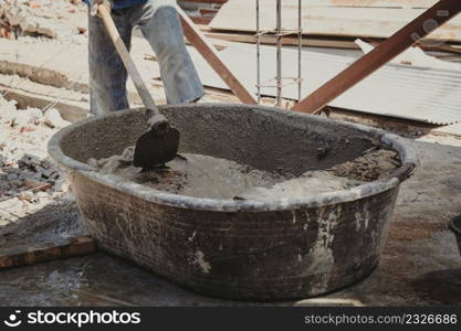 Worker man house builder mix mortar from a trough in bucket