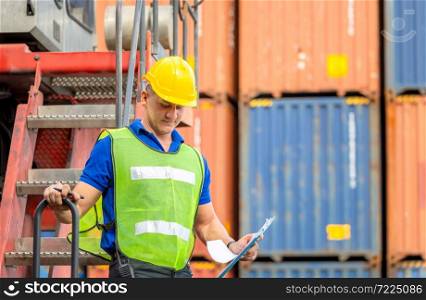 Worker man in hardhat and safety vest standing on container stackers control loading containers box from cargo