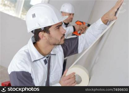 worker mounts sticky tape on wall before painting