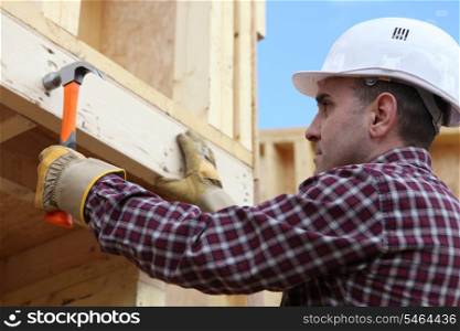 Worker nailing wooden framed house