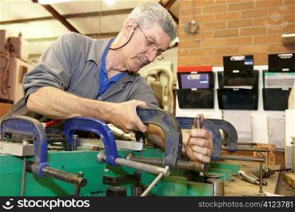 worker on factory floor tightening clamps to secure a machine