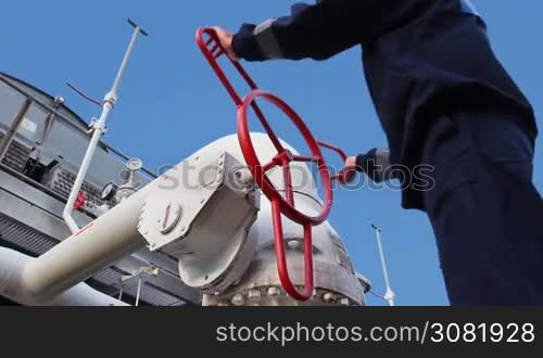 worker opens ball valve on cooling installations at gas compressor station, against background of blue sky, closeup