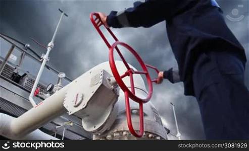 worker opens ball valve on cooling installations at gas compressor station, against background of thunderstorm sky, closeup