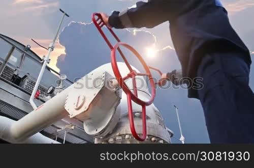 worker opens ball valve on cooling installations at gas compressor station, against background of sunset, closeup