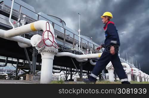 worker opens ball valve on cooling installations at gas compressor station, against background of thunderstorm sky