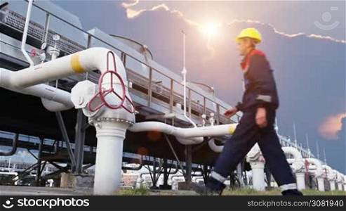 worker opens ball valve on cooling installations at gas compressor station, against background of sunset