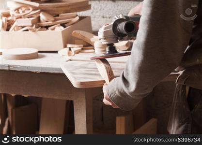 Worker polishing wood table where carpenter hands sanding a wood with electric sander. Sander for wood