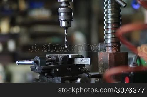 Worker preparing to drill hole in metal workpiece on vertical drilling machine at factory workshop. Man worker fixing workpiece with clamp equipment.