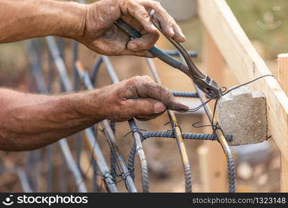 Worker Securing Steel Rebar Framing With Wire Plier Cutter Tool At Construction Site.