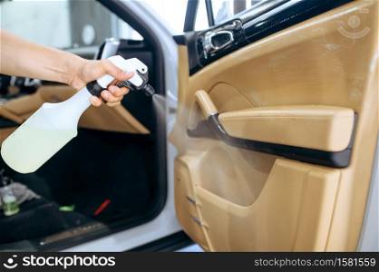 Worker sprays car door trim, dry cleaning and detailing. Vehicle washing in garage, thoroughly care of automobile, chemical and vacuum clean service. Worker sprays car door trim, dry cleaning