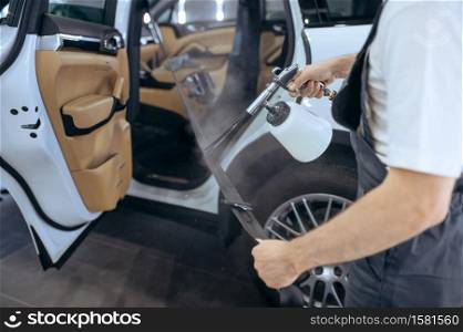 Worker sprays car seat belt, dry cleaning and detailing. Vehicle washing in garage, thoroughly care of automobile, chemical and vacuum clean service. Worker sprays car seat belt, detailing