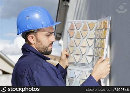 worker standing on step ladder and repairing gutter on house