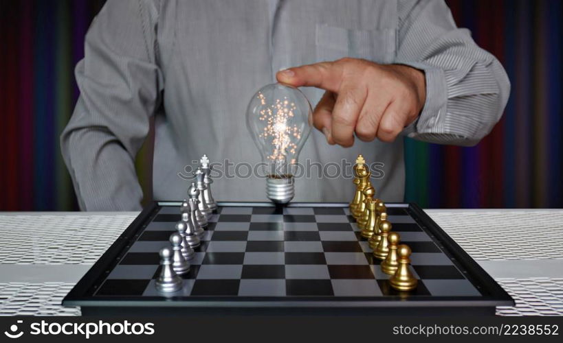 worker touching light bulb on chess board with golden and silver chess pieces
